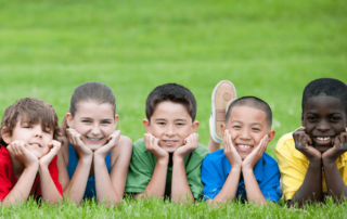 A diverse group of boys and girls with various skin tones smiling and looking at the camera while on a playground at a sports camp, capturing a moment of joy and togetherness.