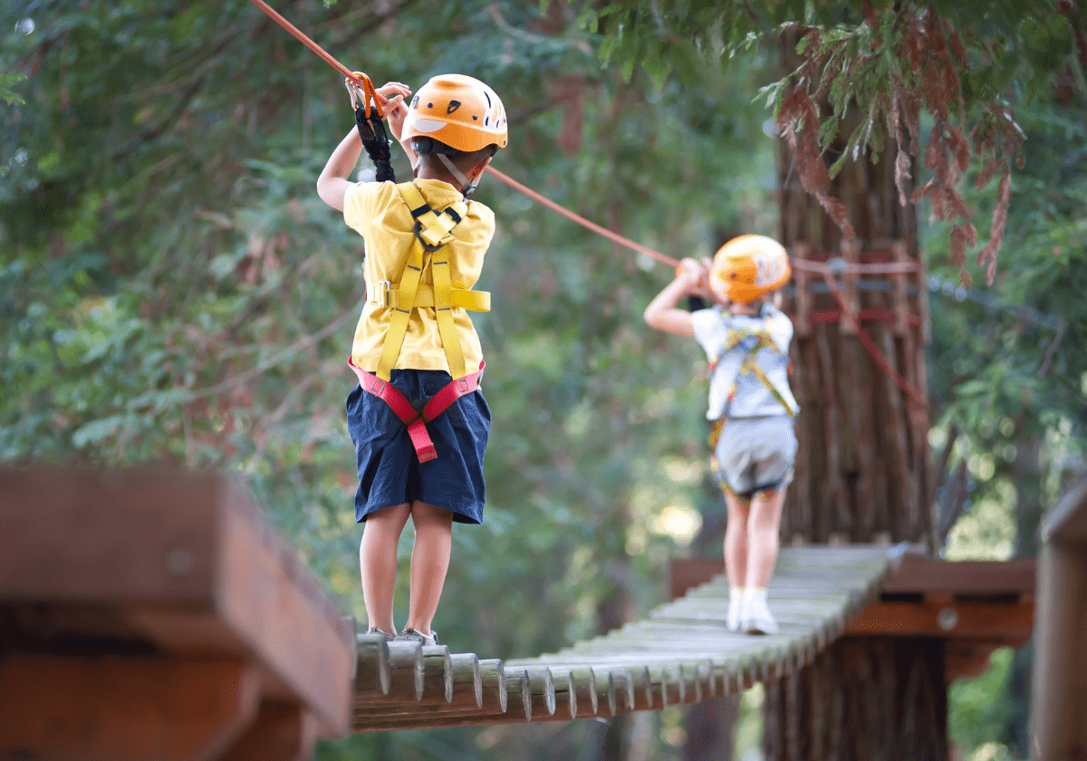 Kids Climbing High Ropes at YMCA Summer Camp Kids wearing helmets while climbing high ropes at a YMCA summer camp, engaging in a safe and adventurous activity that fosters courage and teamwork.