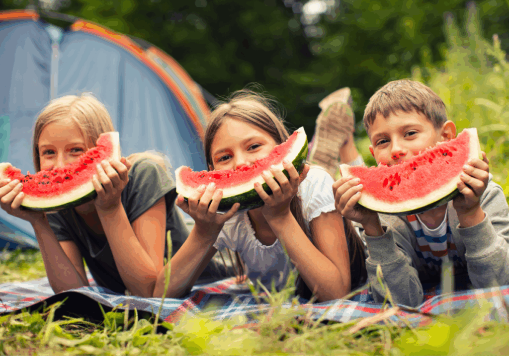 three kids smiling with watermelon in front of tent